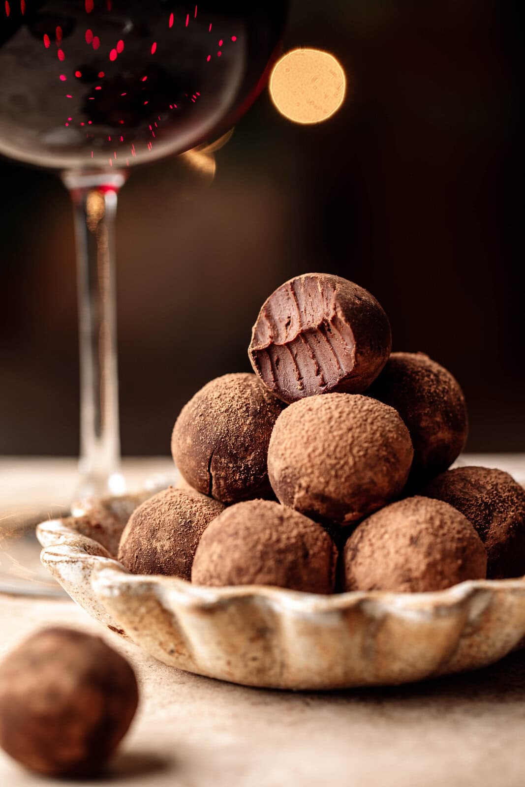 Assorted chocolate truffles on a glass plate with a glass of red wine in the background.