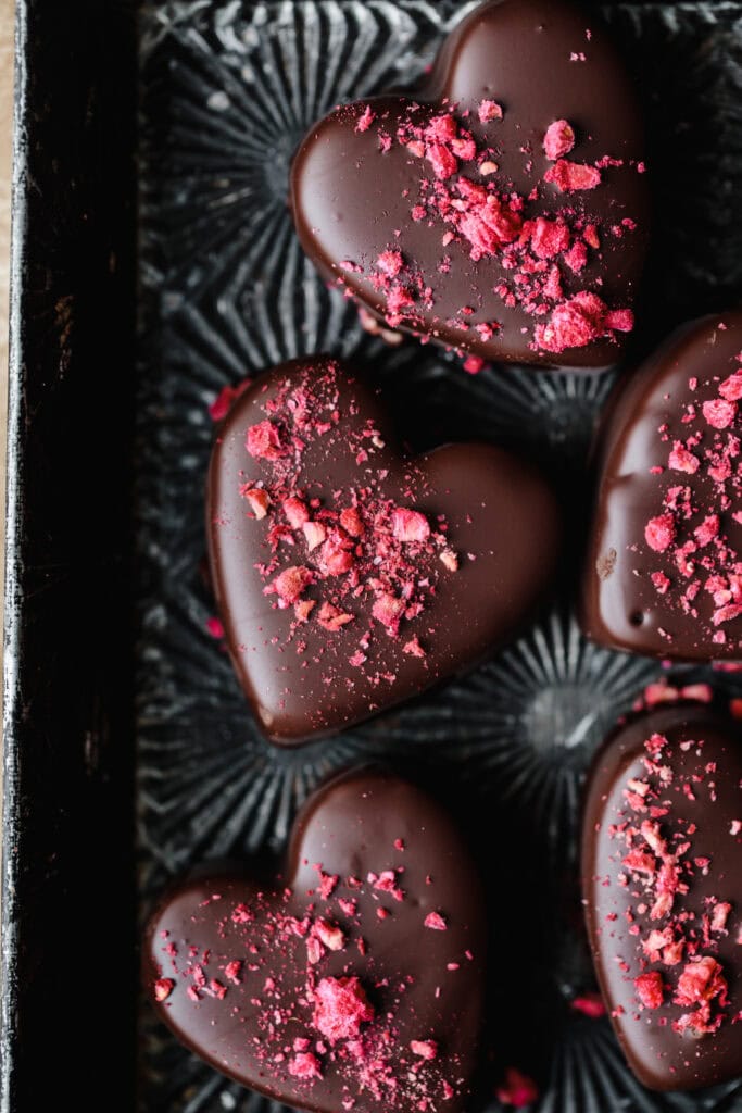 Heart-shaped chocolates with pink sprinkles on a black decorative tray.
