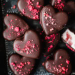 Heart-shaped chocolates with pink sprinkles in a black box.