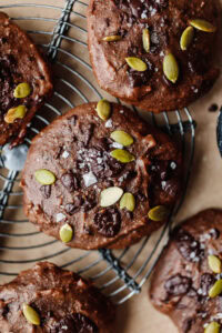 Chocolate muffins topped with pumpkin seeds and sea salt on a cooling rack.