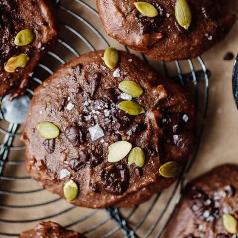 Chocolate muffins topped with pumpkin seeds and sea salt on a cooling rack.