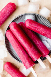 Frozen red fruit popsicles on a black dish with ice cubes around.