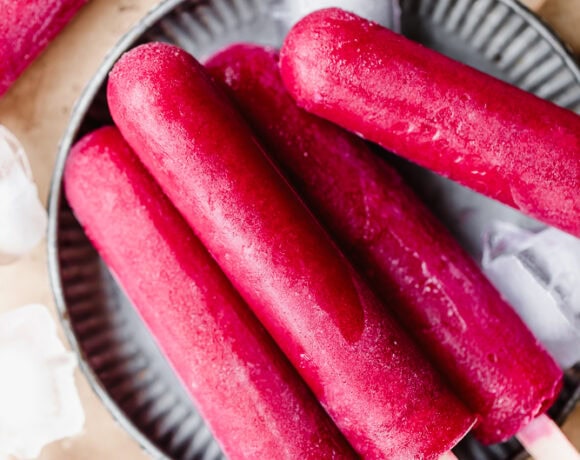 Frozen red fruit popsicles on a black dish with ice cubes around.