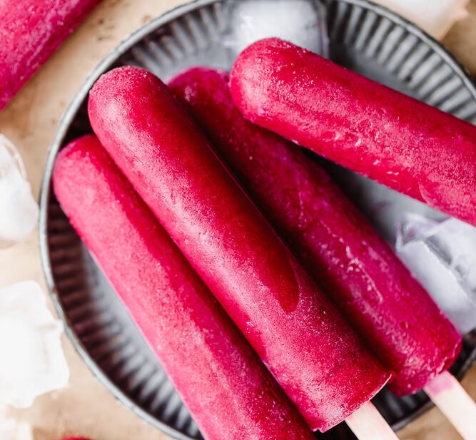 Frozen red fruit popsicles on a black dish with ice cubes around.