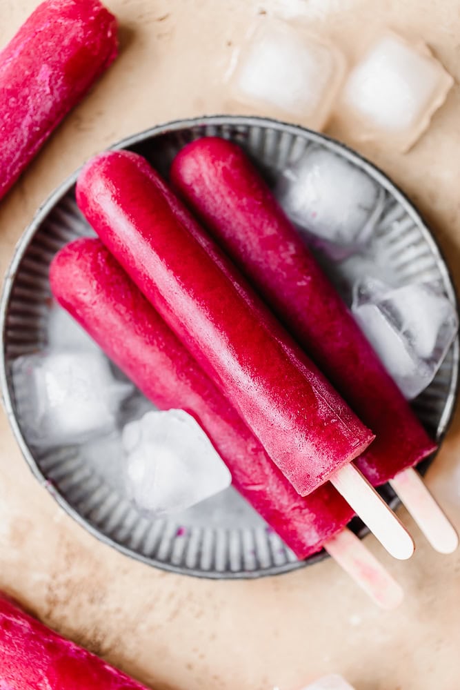 Bright pink fruit popsicles on ice in a metal bowl for a healthy treat.