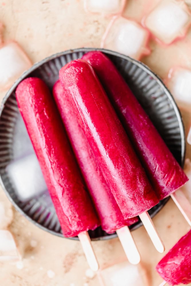Refreshing red fruit popsicles on a black dish with ice cubes around.