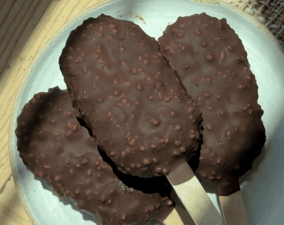 Chocolate ice cream bars with crunchy coating on a white plate.