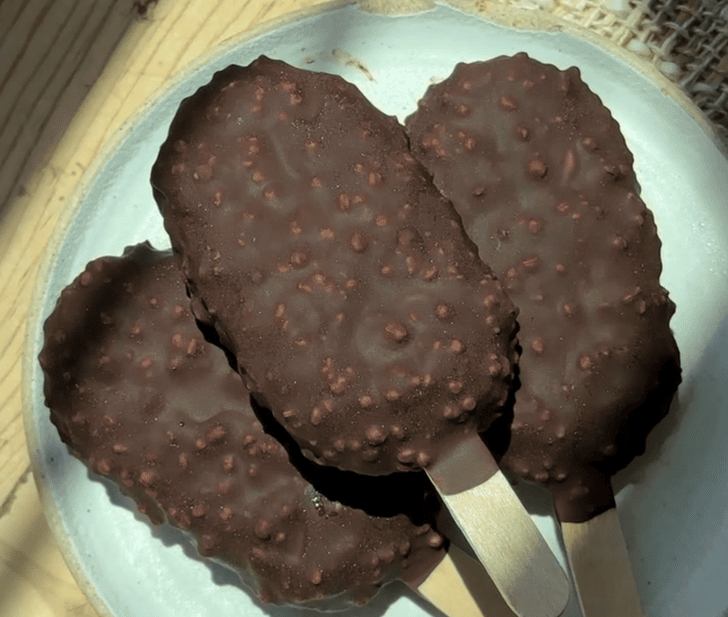 Chocolate ice cream bars with crunchy coating on a white plate.