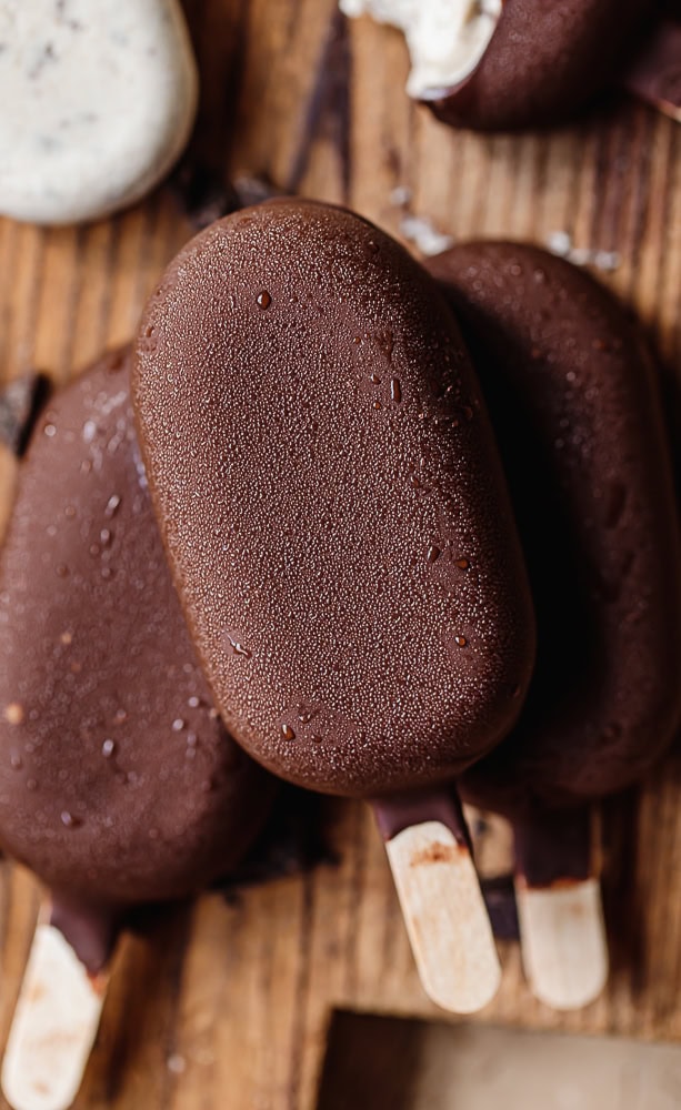 Chocolate ice cream bars with wooden sticks on rustic wooden surface.