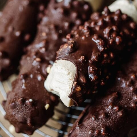 Chocolate-coated ice cream bars with crunchy nuts on a wire rack.