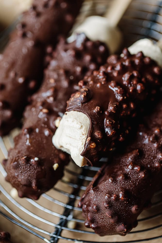 Chocolate-coated ice cream bars with crunchy nuts on a wire rack.