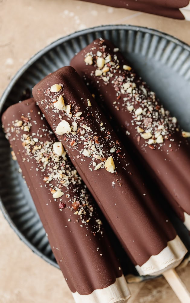 Chocolate ice cream bars with crushed nuts on a black plate.