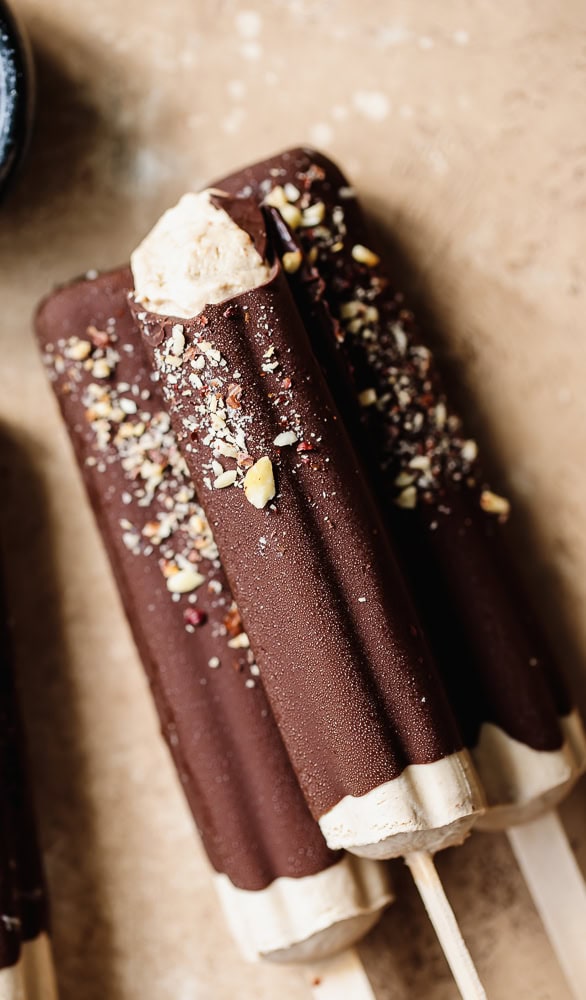 Chocolate ice cream bars with nuts and white coating on wooden sticks.