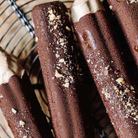 Chocolate ice cream bars with crushed nuts on top, on a wire cooling rack.