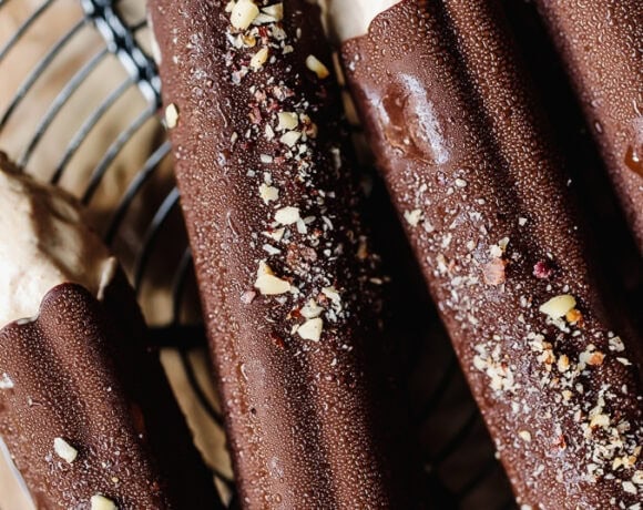 Chocolate ice cream bars with crushed nuts on top, on a wire cooling rack.