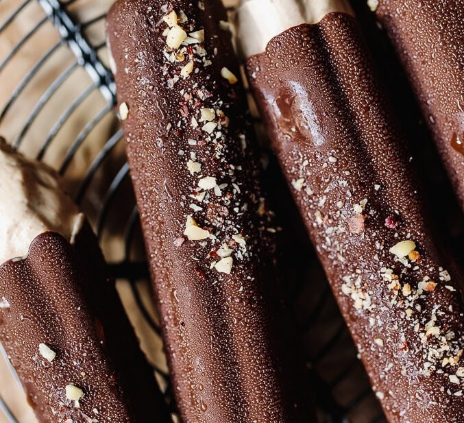 Chocolate ice cream bars with crushed nuts on top, on a wire cooling rack.