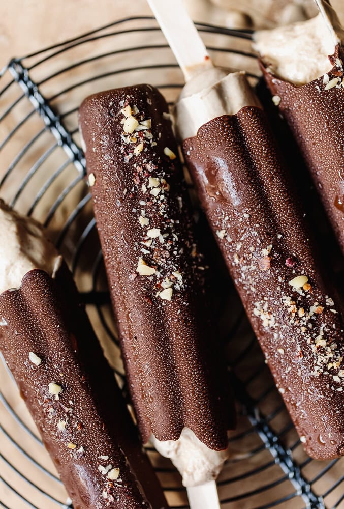 Chocolate ice cream bars with crushed nuts on top, on a wire cooling rack.