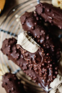 Chocolate-covered protein cookies with crunchy topping on a wire rack.