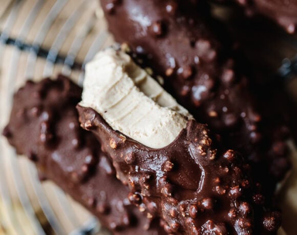 Chocolate-covered protein cookies with crunchy topping on a wire rack.