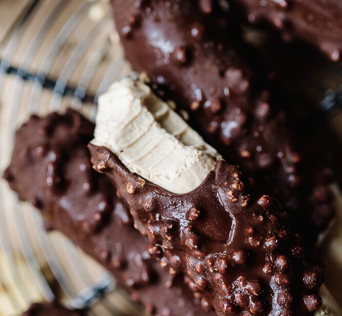 Chocolate-covered protein cookies with crunchy topping on a wire rack.