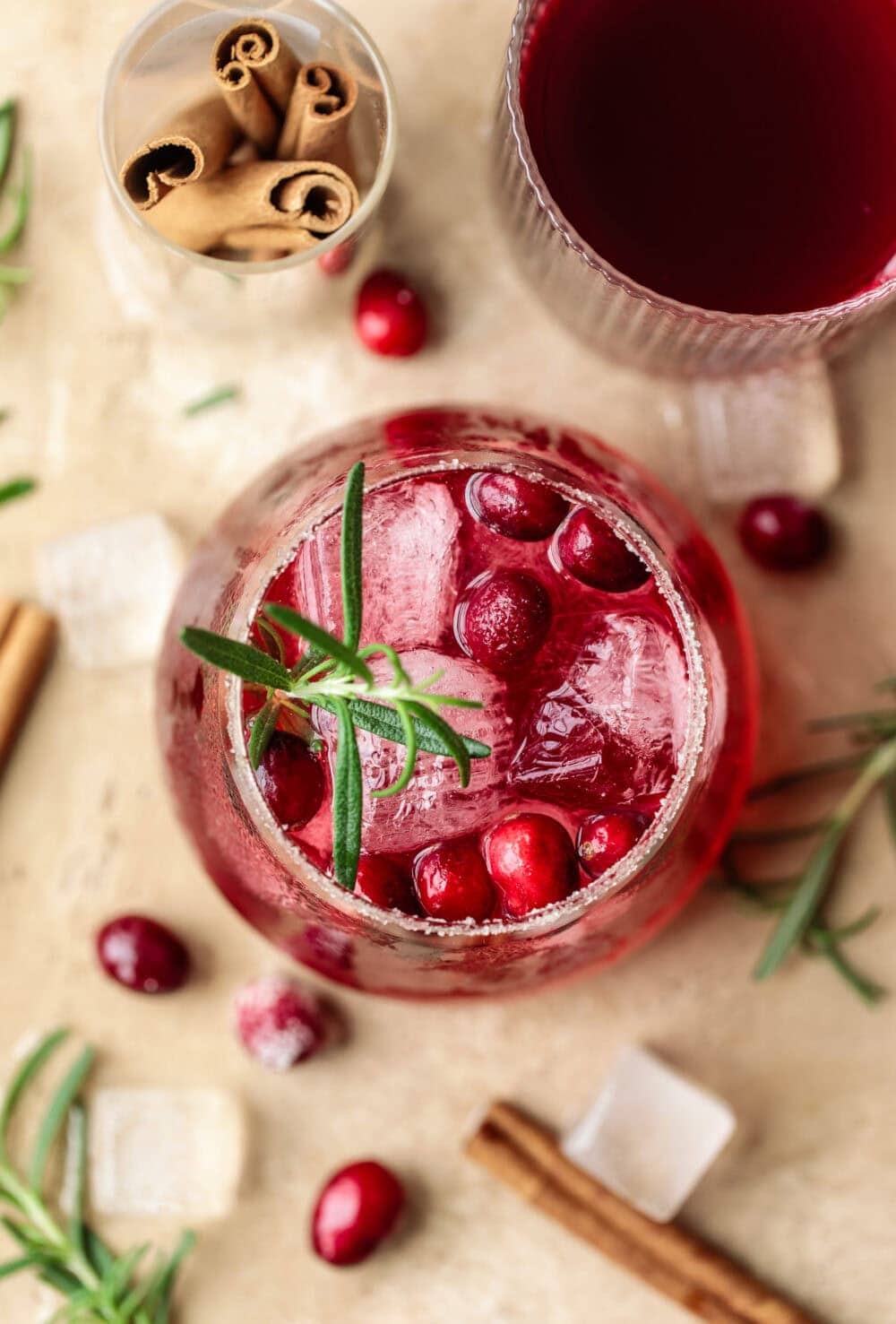 Refreshing cranberry drink with ice and herbs in a glass, festive holiday setting.