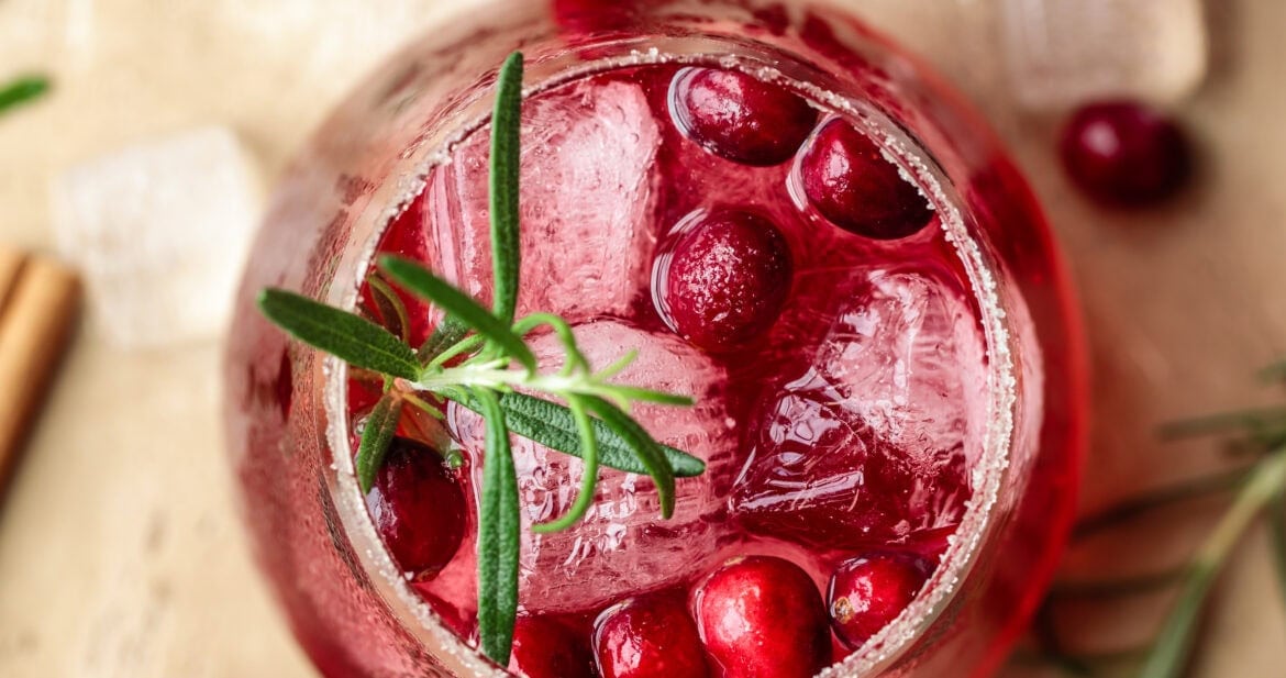 Refreshing cranberry drink with ice and herbs in a glass, festive holiday setting.