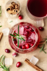 Refreshing cranberry drink with ice and herbs in a glass, festive holiday setting.