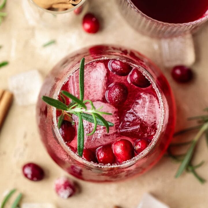 Refreshing cranberry drink with ice and herbs in a glass, festive holiday setting.